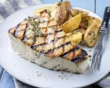 Un succulento trancio di pesce spada alla griglia, guarnito con timo fresco, servito con patate arrosto. Un'idea per le tue prossime ricette di pesce spada.