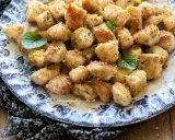 Bocconcini di pollo dorati e croccanti, guarniti con scorza di limone e foglie di menta fresca su un piatto decorato.