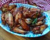 Alette di pollo dorate e croccanti, servite su un piatto decorato con un rametto di rosmarino.