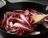 Fette di radicchio rosso vengono saltate in padella con un cucchiaio di legno.