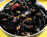 Una ciotola piena di saporita zuppa di cozze, con cozze nere aperte che rivelano la polpa succulenta, condita con erbe fresche e pomodoro.