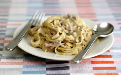 Un piatto di tagliatelle ai funghi cremose, con forchetta e cucchiaio pronti per gustare questo delizioso primo.