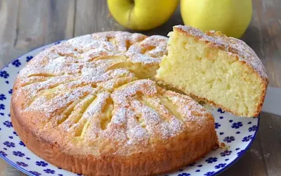 Deliziosa torta di mele con yogurt, cosparsa di zucchero a velo, con una fetta sollevata per mostrare la morbidezza.
