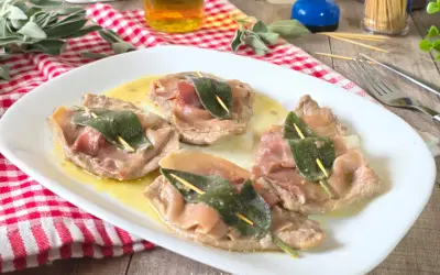 Saltimbocca alla romana su piatto bianco, con prosciutto crudo e salvia, su un tavolo di legno.