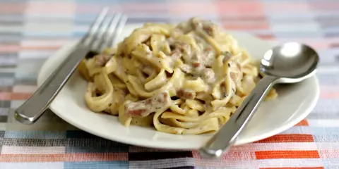 Un piatto di tagliatelle ai funghi cremose, con forchetta e cucchiaio pronti per gustare questo delizioso primo.