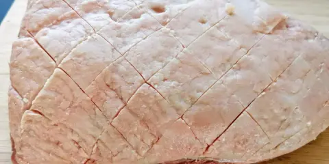 Un pezzo di picanha alla griglia, con la sua copertura di grasso incisa a rombi, pronto per essere cotto su un tagliere di legno.