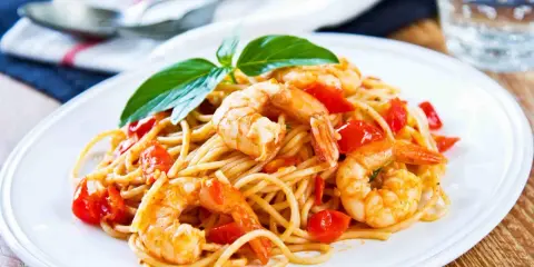 Spaghetti con gamberetti succulenti, pomodorini freschi e basilico, un piatto invitante pronto per essere gustato.