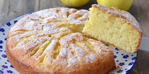 Deliziosa torta di mele con yogurt, cosparsa di zucchero a velo, con una fetta sollevata per mostrare la morbidezza.