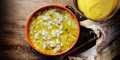 Piatto fumante di baccalà alla vicentina, con polenta gialla e stoccafisso essiccato sullo sfondo.