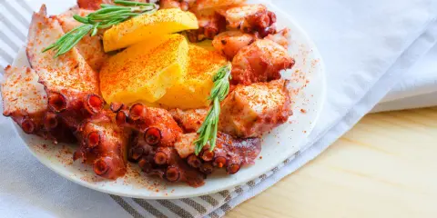 Un invitante polpo alla gallega, cosparso di paprika e guarnito con rosmarino e patate, pronto per essere gustato.