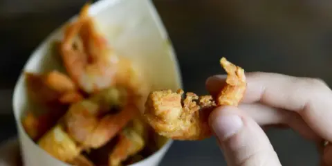 Una mano tiene un gambero croccante, parte di una deliziosa frittura di pesce servita in un cono di carta.