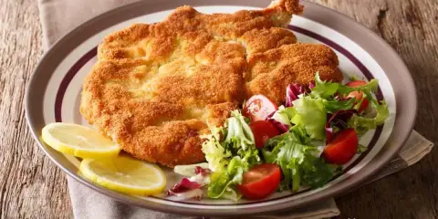 Cotoletta alla milanese dorata e croccante, servita con insalata fresca e spicchi di limone.