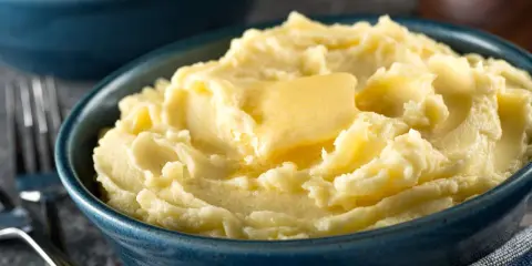 Una ciotola blu piena di soffice purea di patate, con una fetta di burro che si scioglie sopra.