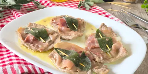 Saltimbocca alla romana su piatto bianco, con prosciutto crudo e salvia, su un tavolo di legno.