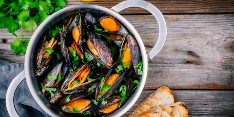 Un pentolino di cozze alla marinara, guarnite con prezzemolo fresco e accompagnate da fette di pane tostato e spicchi di limone.