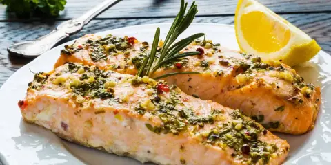 Delizioso salmone al forno con erbe aromatiche, aglio e peperoncino, guarnito con rosmarino e una fetta di limone.