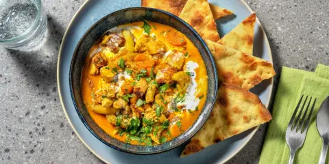 Un invitante pollo al curry cremoso, guarnito con coriandolo fresco e servito con pane naan croccante.