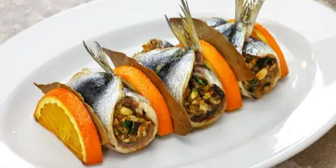 Sarde a beccafico, un piatto siciliano con sardine ripiene, arancia e alloro, servite su un piatto bianco.