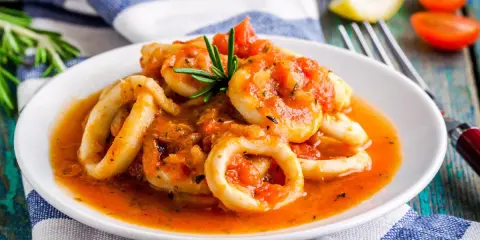 Calamari in umido succulenti, cotti in una salsa rossa saporita, guarniti con rosmarino fresco.