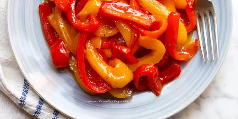 Piatto di peperoni in agrodolce, rossi e gialli, succosi e lucidi, pronti per essere gustati.