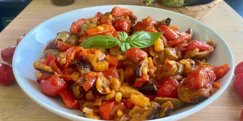 Caponata siciliana ricetta della nonna: melanzane, pomodori, peperoni e basilico in un piatto bianco.