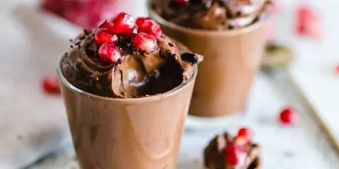 Due bicchierini di golosa mousse al cioccolato, guarniti con chicchi di melagrana e scaglie di cioccolato.