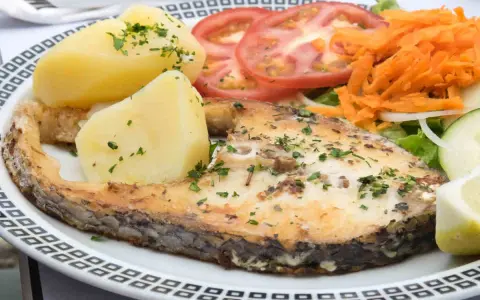 Un succulento pesce spada al forno, accompagnato da patate bollite, pomodori freschi, carote grattugiate e un'insalata leggera.
