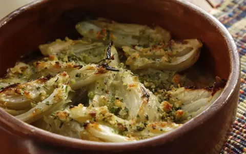 Finocchi al forno dorati e croccanti, conditi con erbe aromatiche e pangrattato, serviti in una terrina di terracotta.