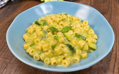 Un piatto di pasta con zucchine e basilico, cremoso e invitante, servito in una ciotola azzurra su un tavolo di legno.