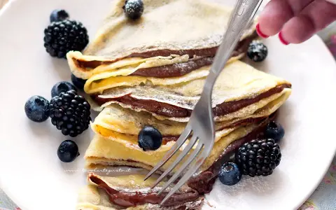 Piatto di crepes alla Nutella, guarnite con mirtilli e more, pronte per essere gustate.