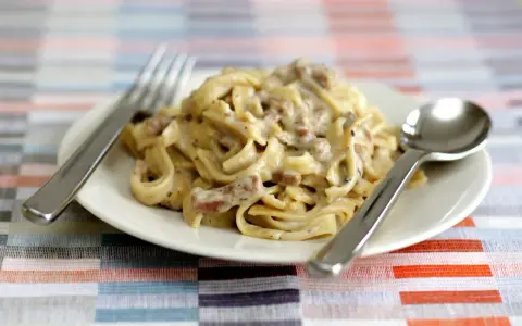 Un piatto di tagliatelle ai funghi cremose, con forchetta e cucchiaio pronti per gustare questo delizioso primo.