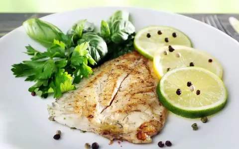Un delizioso filetto di pesce san pietro grigliato, guarnito con erbe fresche, fette di limone e lime con pepe nero.