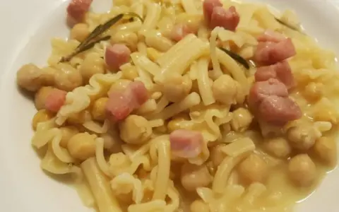 Piatto di pasta e ceci in scatola, con cubetti di pancetta e un rametto di rosmarino.