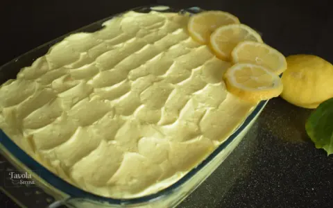 Un invitante tiramisù al limone, guarnito con fette di limone fresco e limoni interi, pronto per essere gustato.