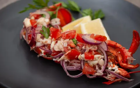 Astice alla catalana: un piatto fresco con astice, pomodoro, cipolla rossa e limone, guarnito con prezzemolo.