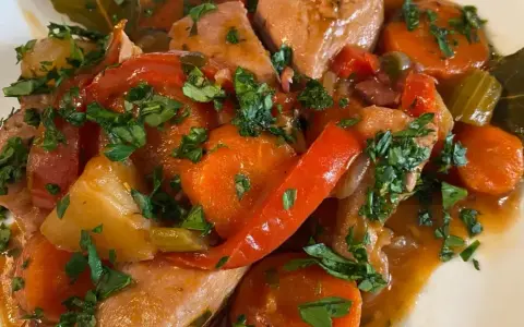 Un saporito spezzatino di pollo con carote, peperoni rossi e prezzemolo tritato, servito in un piatto bianco.