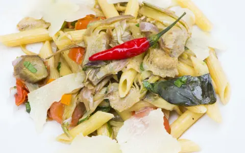 Penne con carciofi, pomodorini, peperoncino rosso e scaglie di parmigiano. Un piatto gustoso e colorato.