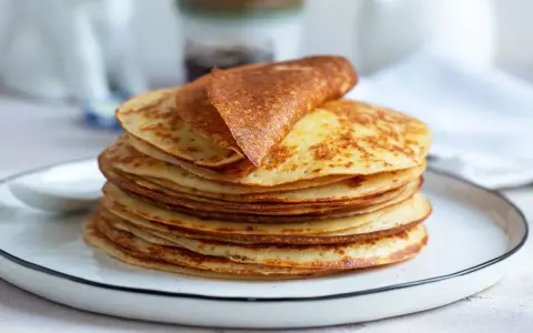 Una pila di dorate crepes senza glutine, una piegata in cima, su un piatto bianco.