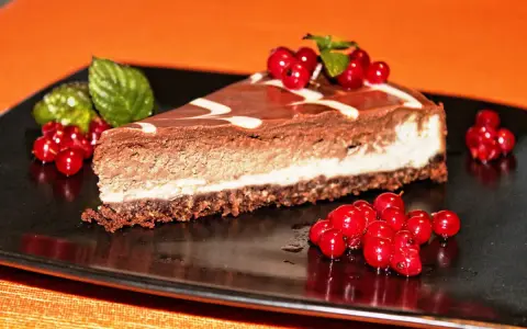 Una fetta di cheesecake alla nutella, con glassa al cioccolato e decorata con ribes rossi e menta.