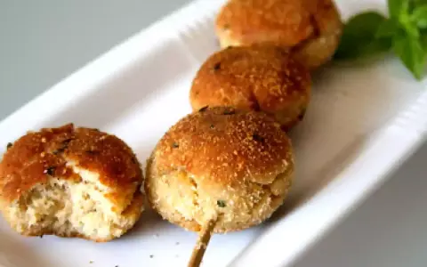 Polpette tonno e ricotta dorate su uno spiedino, una è stata morsa, con basilico fresco.