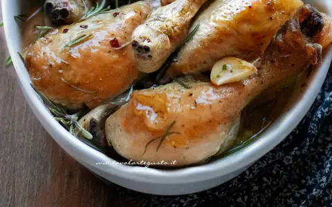Succulente cosce di pollo al forno, dorate e profumate al rosmarino e aglio, servite in una ciotola bianca.