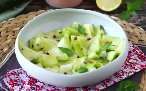 Delicate ribbons of zucchine marinate crude, tossed with fresh mint and pink peppercorns, served in a white bowl.