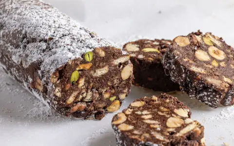 Salame di cioccolato senza uova, ricco di biscotti, nocciole e pistacchi, spolverato di zucchero a velo.