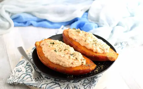 Due patate dolci al forno, tagliate a metà e ripiene di un composto cremoso e speziato, guarnite con erbe aromatiche.