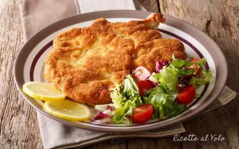Cotoletta alla milanese dorata e croccante, servita con insalata fresca e spicchi di limone.
