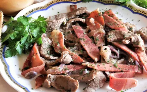 Straccetti di manzo con pancetta e cipolla, guarniti con prezzemolo fresco. Un piatto saporito e invitante.