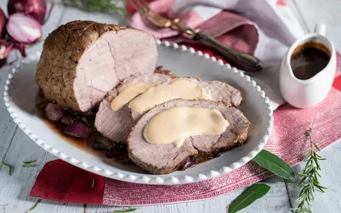 Arrosto di vitello morbido con sughetto benedetta, servito su un piatto bianco con cipolle rosse caramellate e rosmarino.