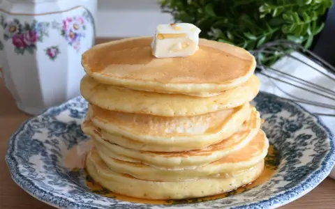 Pila di soffici pancake con farina di avena, guarniti con burro e sciroppo d'acero, su un piatto decorato.