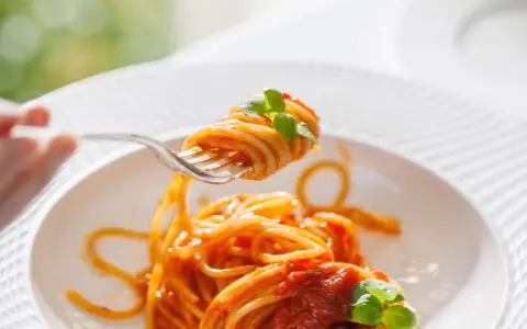 Un primo piatto invitante: spaghetti al dente conditi con un sugo rosso vivo di pomodorini freschi e basilico, pronti per essere gustati.
