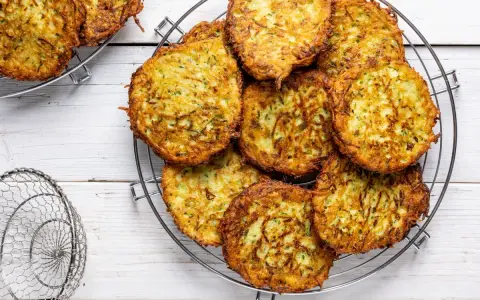 Un mucchio di rosti di zucchine dorati e croccanti su una griglia, pronti per essere gustati.
